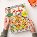 Titelblatt des Magazins „Iss dich GESUND – Besser leben mit Genuss“ mit Foto eines älteren männlichen Arztes in grünem Hemd und Brille oben links sowie einer großen Pizza mit Gemüse und Basilikumblättern im unteren Bereich. Sichtbare Überschriften unter anderem: „Die Super-Kraft der Ballaststoffe“, „Das beste Essen fürs Herz“, „Ernährungs-Doc für zu Hause“ und „Adipositas – Wie Mario 45 Kilo abnahm“. Gehalten von zwei Händen über hellem Tisch.