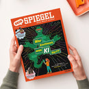 Orangefarbenes „DEIN SPIEGEL“-Magazin mit dem Untertitel „Durch Wissen wachsen“, schräg auf weißer Fläche von zwei Händen gehalten. Das Cover zeigt einen grünen Roboter auf schwarzem Hintergrund mit bunten Linien und dem Titel „Wer bestimmt, was KI darf?“ sowie die Texte „IM INTERVIEW Zehnkämpfer Leo Neugebauer“, „IM SATTEL Viktoria Huld, 13, trainiert Pferde“ und „Von Fake News bis Fake Freunde – warum wir jetzt kluge Regeln brauchen“.