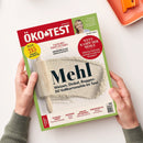 Titelblatt der Zeitschrift „ÖKO-TEST“ mit rotem Logo und weißem Schriftzug, gehalten von zwei Händen über hellem Hintergrund. Auf der Mitte liegt abgebildetes Mehl mit Holzrolle, dazu der Haupttitel „Mehl – Weizen, Dinkel, Roggen: 50 Vollkornmehle im Test“. Weitere Texte: „TEST 215 Produkte für jeden Tag“, „Wettkampf der Mehle“, „Oster-Eierfarben“, „Babybäder“, „Kräuter der Provence“ und ein Interview mit einer blonden Frau im oberen Bereich.