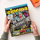 Titelblatt der Zeitschrift „cinema“ Ausgabe 5/25, mit großem gelben Schriftzug oben und Überschrift „DIE NEUEN BLOCKBUSTER“ auf schwarzem Balken. Mehrere Filmszenen und Figuren aus unterschiedlichen Genres sind in farbigen Bildfeldern angeordnet, ergänzt durch Textzeilen wie „IM CHECK! +52 Kinofilme“ und Hinweise auf Interviews zu „THE LAST OF US“. Gehalten von zwei Händen über hellem Hintergrund, oben rechts orangefarbene Ablagebox sichtbar.