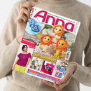 Person in beigefarbenem Strickpullover hält das Magazin „Anna“ (Ausgabe Juni 2025) mit dem Titel „Ideen zum Selbermachen – Kreativ und aktuell“. Auf dem Cover sind drei gehäkelte Löwenfiguren mit orangefarbener Mähne abgebildet, daneben kleinere Fotos von Strick- und Häkelprojekten, u. a. eine Frau in pinkem Oberteil, ein Garnknäuel sowie das Textfeld „So schön wird der Sommer!“, weitere Textfelder zu „Granny Square-Tier“, „Modestrick“ und „Lehrgang“.