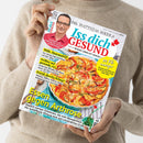 Hellhäutige Person in beigefarbenem Strickpullover hält eine Zeitschrift mit dem Titel „Dr. Matthias Riedl’s Iss dich GESUND – Besser leben mit Genuss“. Auf dem Cover oben ein Porträtfoto eines Mannes mit Brille und rotem Hemd, darunter ein Teller mit überbackenem Gemüsegericht. Sichtbare Schlagzeilen: „Essen gegen Arthrose“, „Hilfe, Haarausfall!“, „Grillen auf gesunde Art“, „Krank durchs Klima?“ und gelber Kreis mit „50 Kilo weniger“.