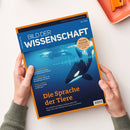 Titelblatt der Zeitschrift „Bild der Wissenschaft“ Ausgabe 06/2025 mit blau-orangefarbenem Randdesign. Im Zentrum ein Unterwasserbild mit zwei Orcas in stilisierter Schallwellenoptik. Textelemente: Haupttitel „Die Sprache der Tiere“ und Unterzeile über Künstliche Intelligenz in der Biologie, weitere Themen in kleiner Schrift links, gelber Kreis mit Hinweis „Neue Serie Wasserstoff: Der große Umbau“. Gehalten von zwei Händen über hellem Tisch.
