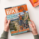 Titelbild der Zeitschrift „MountainBIKE“ mit orangem Kopfbereich und großem weiß-orangem Schriftzug. Im unteren Bereich zwei männlich gelesene Personen mit Helmen und Mountainbikes in bergiger Landschaft, eine Person trägt orange-blaue Radkleidung, die andere olivgrün. Sichtbare Überschriften: „Das große Bosch-Update“, „Alles Enduro“, „32 Zoll – kommt jetzt die nächste Welle?“, „Rucksack-Check“, „Neue E-MTBs“, „Tour Royal“.