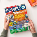 Magazin „PC-WELT+“ Ausgabe 6 / 2025 mit überwiegend orangefarbenem Titelbereich; zentrale Schlagzeilen: „Windows Update-Garantie“, „Sicherheit XXL“, „Linux ganz einfach“, „Lokale KI‑Tools“. Weitere Textfelder in Blau, Gelb, Lila und Grün, darunter Abbildungen eines Laptops, einer DVD, von Software‑Icons und Logos. Gehalten von zwei Händen über hellem Tisch, oben Teil eines orangefarbenen Tabletts sichtbar.