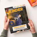 Titelblatt des Magazins „Servus Kinder“, gehalten von zwei Händen über hellem Untergrund. Im Zentrum eine gezeichnete graue Maus im blauen Trenchcoat und Hut mit Sonnenbrille, stehend in nächtlicher Gasse mit Laternenlicht. Überschriften oben: „Forschen & Fragen“, „Erleben & Entdecken“, „Lachen & Rätseln“, „Basteln & Kreativ sein“. Textfeld unten: „STRENG GEHEIM! Verborgene Botschaften und Goldbarren im Tresor…“.