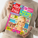 Eine Person in beigefarbenem Strickpullover hält eine Ausgabe der Frauenzeitschrift „Alles für die Frau“. Das Cover zeigt eine lachende blonde Frau vor gelbem Hintergrund, umgeben von Texten wie „1 Kilo weg über Nacht“, „Backen mit Kaffee“, „Spar-Sommer“, „Super-Wochenplaner“ und „Riesen-Rätsel-Spaß“ in bunten Textfeldern in Blau, Gelb, Pink und Rot.