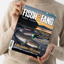 Person im beigefarbenen Strickpullover hält eine schräg fotografierte Zeitschrift mit dem Titel „FISCH & FANG“ und der Aufschrift „Das Erlebnis-Magazin für Angler“; auf dem Cover liegen mehrere silberfarbene Fische auf schwarzer Angelausrüstung. Sichtbare Texte: „Meeresangeln“, „Allein am Wasser“, „Fischküche“, „Trotting am Fluss“, „Rund ums Dekor“, „Heißes Deadbaiten“ und „Alle lieben Würmer“.