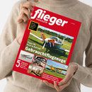 Weibliche Person im beigefarbenen Strickpullover hält ein schräg abgebildetes rotes Magazin mit dem Titel „flieger MAGAZIN“. Sichtbare Texte: „Was ein Flugzeug wirklich kostet“, „Tipps für Kauf & Betrieb Gebrauchtflugzeuge“, „5 Flugzeug-Porträts: Cessna, Piper & Co.“ sowie „Einsteiger-Gebrauchte · Haltergemeinschaft · UL-Geheimtipps · Finanzierung“; mehrere Fotos von Kleinflugzeugen ergänzen das Cover.