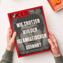 Rot umrandetes FOCUS-Magazin in schräger Perspektive auf weißer Fläche, von zwei Händen einer nicht näher erkennbaren Person gehalten; grauschwarzes Titelmotiv mit großer weißer Aufschrift „WIE TROTZEN WIR DER ISLAMISCHEN GEFAHR?“. Sichtbare Texte: „Endspiel für den Kanzler“, „Wirtschaft unter Schock“ und „ADC GRAND PRIX 2024 // EUROPEAN PUBLISHING AWARDS WINNER 2026“; oben rechts liegt ein orangefarbener Bürogegenstand.