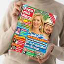 Weibliche Person im cremefarbenen Strickpullover hält eine schräg betrachtete Zeitschrift mit dem Titel „Frau mit Herz“. Das farbige Cover zeigt eine blonde Frau und einen bärtigen Mann mit Hut sowie die Texte „Beatrice Egli: Baby-Sehnsucht“, „Süße Pläne fürs Familienglück“, „Florian Silbereisen: Angriff! Schlager-Stars packen aus!“, „Stefanie Hertel und ihr Lanny: Ihr aufregendes Ehe-Rezept“ und „Picknick-Ideen“.