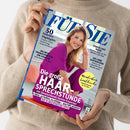 Hochkant gehaltene Zeitschrift „Für Sie“ mit blauem Titel auf hellem Cover; davor eine blonde Frau in pinker Kleidung, im Hintergrund eine Person im beigefarbenen Strickpullover. Sichtbare Texte: „50 Sommer-Highlights“, „Tropical-Prints“, „Badeanzüge“, „Sonnenbrillen & Co.“, „Die große Haar-Sprechstunde“, „Stress lass nach!“ und „Die Liebe auffrischen“.