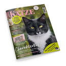 Schräg fotografierte Ausgabe des Katzenmagazins „Geliebte KATZE“ auf schwarzem Hintergrund, mit großem schwarz-weißem Katzenporträt, kleinem hellen Kätzchen links und eingerahmtem grau getigertem Kater. Sichtbare Texte: „Europas beliebtestes Katzenmagazin“, „Aktuelle Forschung: Wie Katzen uns gesünder machen“, „Experten-Tipps“, „Pinkel-Pannen“, „Charakterkopf“, „Psycho-Test“ und „Zum Weltkatzentag“.