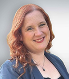 Porträt einer lächelnden Frau mit roten Haaren, sie trägt einen blauen Blazer.