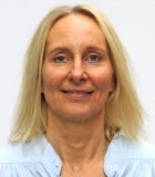 Porträt einer blonden Dame. Sie schaut in die Kamera und lächelt.