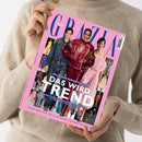 Eine Person im beigefarbenen Strickpullover hält ein schräg ausgerichtetes, pinkfarbenes Magazin mit dem Titel „GRAZIA“ und „DAS WIRD TREND“. Auf dem Cover sind drei Models in Denim, roter Lederkleidung und rosafarbenem Kleid sowie Modefotos abgebildet; sichtbare Texte: „DIE GROSSE RUNWAY-EDITION“, „LEDER-STYLES +++ DOUBLE-DENIM +++ NEW-WHITE +++ OVERKNEES +++ GOTHIC-GLAM“ und „IM SPOTLIGHT: Charlize Theron + Sienna Miller + North West + Blake Lively“.
