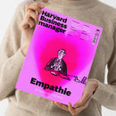 Eine Person im beigefarbenen Strickpullover hält ein einzelnes, leicht schräg fotografiertes Magazin mit pink-lilafarbener Oberfläche und schwarzer Illustration einer sitzenden Person. Aufschrift: „DAS WISSEN DER BESTEN Harvard Business Manager“, „Empathie – Die Superkraft in der Krise“, HBR sowie „Preissenkungen“, „Einsteigerjobs“, „Stakeholder“ und „Überlastung“.