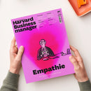 Magenta-pinke Ausgabe des „Harvard Business manager“ mit schwarzem Titel „Empathie“ und dem Untertitel „Die Superkraft in der Krise“, gehalten von zwei Händen über weißem Hintergrund. Das Cover zeigt eine gezeichnete männliche Person im Anzug an einem Schreibtisch mit Herzsymbol; sichtbar sind außerdem „Das Wissen der Besten“, „HBR“ sowie Themenhinweise zu Preissenkungen, Stakeholdern, KI und Überlastung.