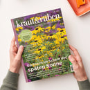 Zeitschrift „kraut&rüben“ mit dem Untertitel „SCHÖNER. WILDER. BIOGARTEN.“ auf einem farbigen Foto gelber Blüten, gehalten von zwei Händen; sichtbar sind grüne Pflanzen, violetter Hintergrund und violetter Rand. Lesbare Titel: „COOL-FLOWER-METHODE: Jetzt säen, im Frühling strahlen“, „Die Tomaten sind reif!“ und „Gärtnern im Schein der späten Sonne“.