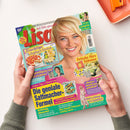 Schräg liegende, farbig gedruckte „LISA“-Zeitschrift auf weißer Fläche, von zwei Händen mit grauen Strickärmeln gehalten; auf dem Cover eine blonde Frau sowie die Texte „Mit Liebe gemacht!“, „Fruchtige Joghurt-Torten“, „Ist Ihre Lymphe im Fluss?“, „Frische fürs Zuhause“ und „Die geniale Sattmacher-Formel“. Oben rechts liegen ein orangefarbenes Tablett und ein orangefarbenes Bürogerät.