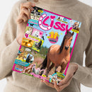 Eine Person im beigefarbenen Strickpullover hält ein schräg fotografiertes „Lisa“-Magazin mit pinkem Rand vor weißem Hintergrund. Das Cover zeigt ein braunes Pferd, mehrere kleinere Pferdefotos und Illustrationen sowie die Texte „REPORT“, „BACKSTAGE BEIM Reitturnier“, „COOLER GEWINN!“, „FOTOROMAN“, „4 POSTER ZUM VERLIEBEN“, „DIY Pferdestärke ABKÜHLUNG“, „ZUM WIEHERN KOMISCH“, „Welcher Pferde-Typ passt zu dir?“ und „Retro Comic“.