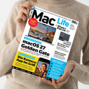Eine Person im beigefarbenen Strickpullover hält eine schräg ausgerichtete Zeitschrift „Mac Life“ mit weißem Cover. Sichtbare Texte: „iPhone Ultra“, „macOS 27 Golden Gate“, „Die Kamera-App im Griff“, „iPhone & iPad Life“ und „Nie wieder fiese Abo-Kosten“; abgebildet sind ein MacBook, ein iPhone, ein Lautsprecher und ein Mac-Zubehörgerät.