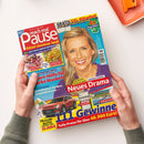 Zeitschrift „Pause“ mit rotem und türkisfarbenem Cover, gehalten von zwei Händen. Darauf eine lächelnde blonde Frau sowie die Texte „Rätsel Gewinnen Spaß“, „GRATIS XXL-Rätselteil“, „Neues Drama“ und „111 Gewinne“; abgebildet sind außerdem Rätsel, Speisen, ein Auto, ein Grill und eine Landschaft.