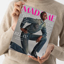 Beige gestrickter Pullover hält ein schräg liegendes graues „MADAME“-Magazin. Das Cover zeigt ein männliches Model mit dunkler Haut in blauem Denim-Outfit und schwarzen Schuhen; sichtbare Texte: „ENDLICH FIT“, „Leicht & straff mit dem richtigen Krafttraining“, „WELT RÄUME“, „Die jungen Meister des Interior-Designs“ und „RELAX! So lässig ist die neue Mode“.