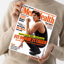 Weiße „Men’s Health“-Zeitschrift mit orangefarbener und schwarzer Typografie, gehalten von den Händen einer Person im beigefarbenen Strickpullover. Auf dem Cover: eine männliche Person in schwarzer Sportkleidung sowie die Texte „Selbst-Check: Bin ich schon wie mein Vater?“, „Longevity-Food: Lecker essen, länger leben“, „Nicholas Galitzine“, „Das stärkt dein Herz“ und „Fit in nur 21 Tagen“.
