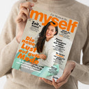 Hochformatige Zeitschrift „myself“ mit orangefarbener Titelgestaltung, gehalten von einer weiblichen Person in beigefarbenem Strickpullover. Das Cover zeigt eine dunkelhaarige Frau in weißer Kleidung und türkisfarbener Hose sowie die Texte „Ein Moment für …“, „Zeit zu lesen!“, „Die neue Lust auf gute Mode“, „Paare begegnen sich selten wirklich“, „Sie werden STAUNEN, wie gut es sich anfühlt“ und „Wohnen mit Stil“.