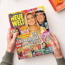 Auf weißem Untergrund hält eine Person mit grauen Ärmeln eine schräg liegende Zeitschrift. Das Cover zeigt den Titel „NEUE WELT FÜR DIE FRAU“, eine blonde Frau und einen Mann mit Hut und Brille sowie kleinere Porträts; lesbare Schlagzeilen sind „EIN LEBENSZEICHEN von ihrer Tochter“, „AL BANO & ROMINA“, „Ylenia verschwand vor 32 Jahren“, „Sommer des Glücks“ und „Kampf zurück ins Leben“.