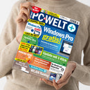Person ohne sichtbares Gesicht und mit nicht erkennbarem Geschlecht hält mit beiden Händen schräg die Zeitschrift „PC-WELT plus“ vor einem hellbeigen Strickpullover. Das Cover zeigt unter anderem die Texte „2 DOPPEL-DVDs“, „Windows Pro gratis!“, „Update mit 1-Klick“, „WLAN-Tuning“, „Ihr Recht auf Reparatur“ und „Download-Check-DVD“ sowie Abbildungen von Laptop, Softwarefenstern, DVDs und Routern.