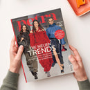 Schräg von oben fotografierte, aufgeschlagene „petra“-Zeitschrift in zwei Händen auf weißer Oberfläche. Das Cover zeigt drei weibliche Models in schwarzer, roter und blauer Kleidung sowie die Texte „Mein Leben! Mein Luxus!“, „DIE NEUEN TRENDS“, „DER NEUE STOFFWECHSEL-CODE“ und „BRETONISCHE GEHEIMNISSE“.
