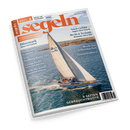Schräg liegendes Magazin „segeln“ mit weißem Rand und orange-blauem Titelblatt; darauf ein weißes Segelboot mit gesetzten beigefarbenen Segeln auf blauem Meer vor einer Küstenlandschaft. Sichtbare Texte: „Juli/August 2026“, „Mensch über Bord“, „Dänemark“, „Deckssalon im Eigenbau“, „Test: Hallberg Rassy 370“, „Werft für Selbstmacher“ und „8 Seiten Gebrauchtboote“.