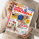 Eine Person in beigefarbenem Strickpullover hält eine schräg fotografierte Zeitschrift mit dem roten Titel „selber machen“ und gelbem „DIY Do it yourself“-Logo. Das Cover zeigt Handwerks- und Renovierungsszenen sowie Texte wie „Grill mauern“, „Praxistest“, „Platzsparende Balkon-Bar“, „Neue Badideen“ und „So gelingt Ihnen glatte Wände“.
