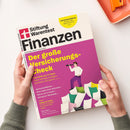 Schräg gehaltenes Finanzmagazin „Stiftung Warentest Finanztest“ mit weißem und magentafarbenem Cover, schwarzer Titelzeile „Finanzen“ und gelbem Hinweis „Frist für Steuererklärung“. Auf dem Cover stehen „Der große Versicherungs-Check“ sowie „Top-Tarife aus 11 Tests: Teure Verträge kündigen, wechseln und sparen“; zwei Hände mit grünen Strickärmeln halten das Magazin vor weißem Hintergrund.