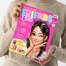Hände und Oberkörper einer Person halten eine schräg abgebildete Zeitschrift mit pinkem Cover „TOPModel FRIENDS Club“. Darauf: eine gezeichnete weibliche Figur mit dunklem Haar und großer lila Schleife sowie Texte wie „Medienzeit: Sicher unterwegs im Internet“, „Beste-Freundinnen-Sommer“, „Neu im Club?“ und „Deine EXTRAS: über 150 Sticker und viele Ausmalbilder“.