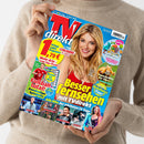 Weibliche Person in einem beigefarbenen Strickpullover hält eine schräg ausgerichtete Zeitschrift mit blauem Cover. Sichtbare Texte: „TV direkt“, „Besser essen mit TV direkt“, „Fußball total!“, „Fett-weg-Formel“, „Superkräfte der Tiere“, „Mediatheken-Planer“ und „Alle Hits der nächsten 14 Tage“; das Cover zeigt eine blonde Frau sowie kleinere Sport-, TV- und Tierbilder.